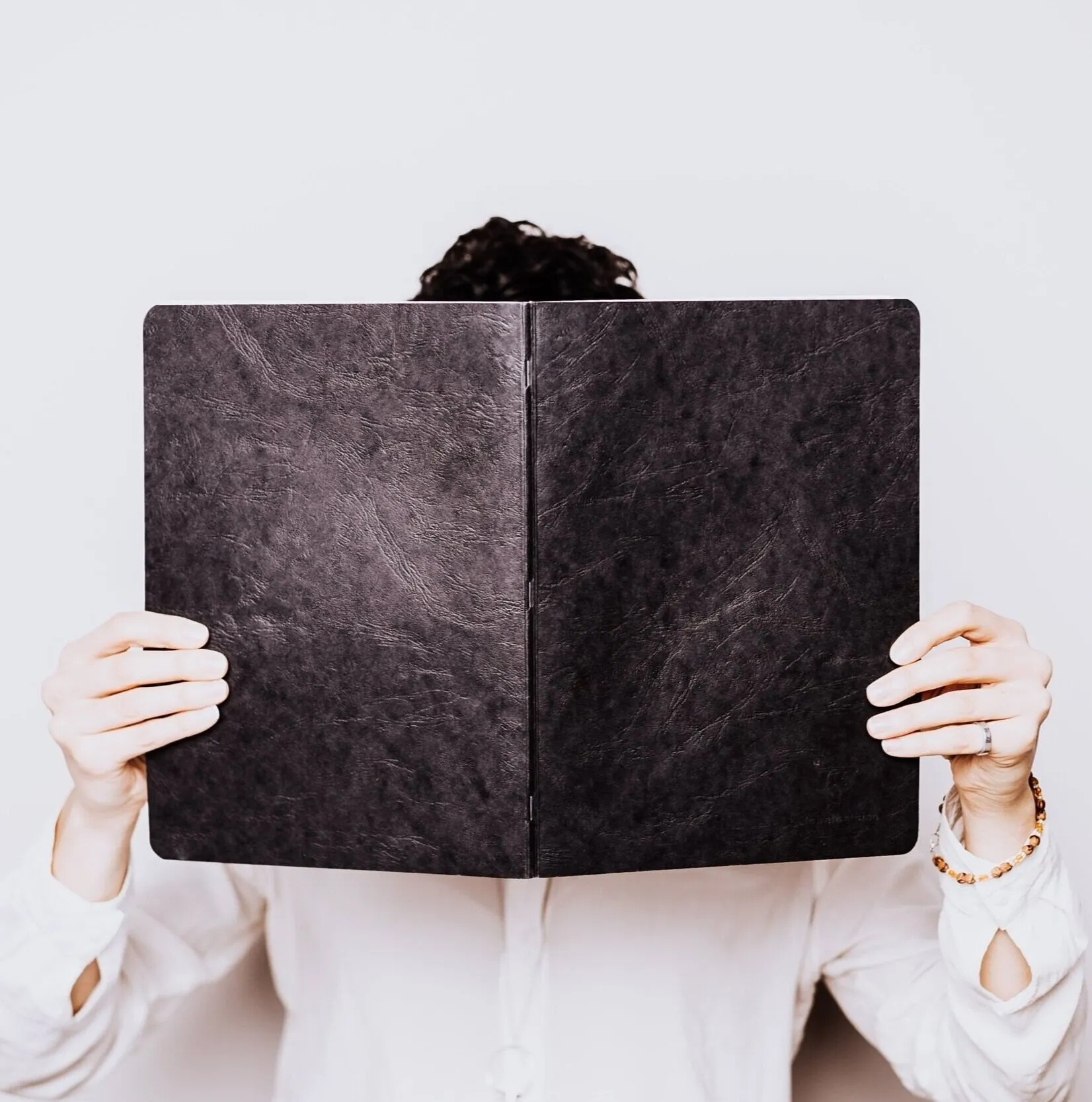 A person holding a large black notebook in front of their face