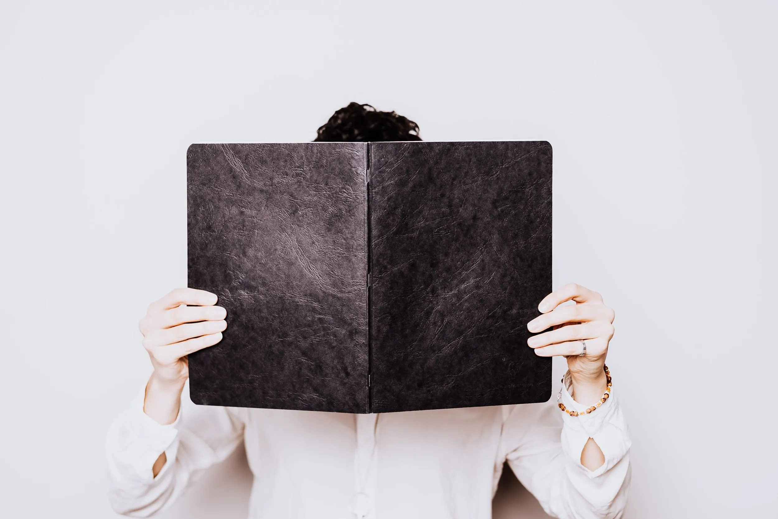 A person holding a large black notebook in front of their face