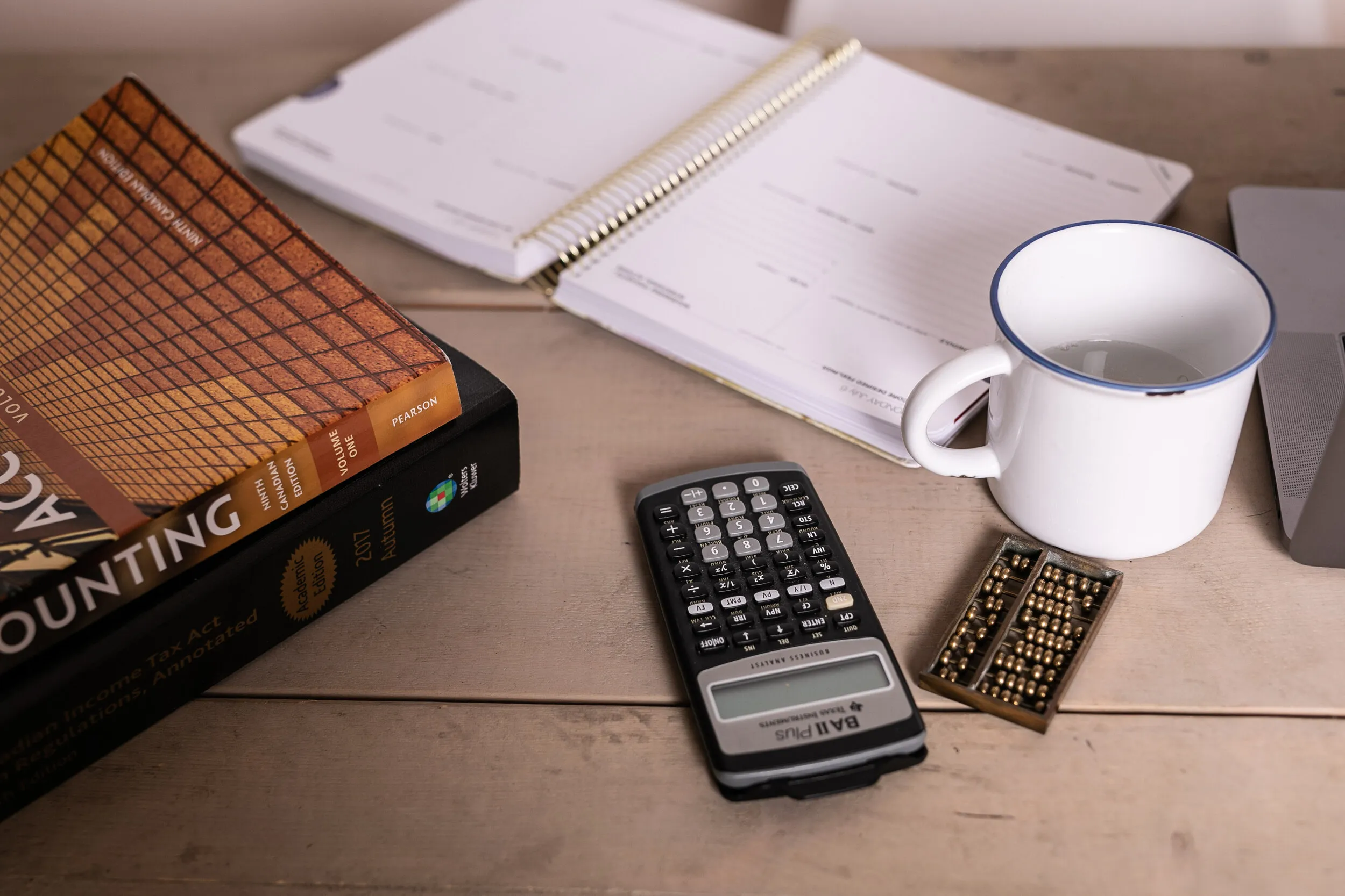 A desk with a notebook, calculator, abacus and enamel mug
