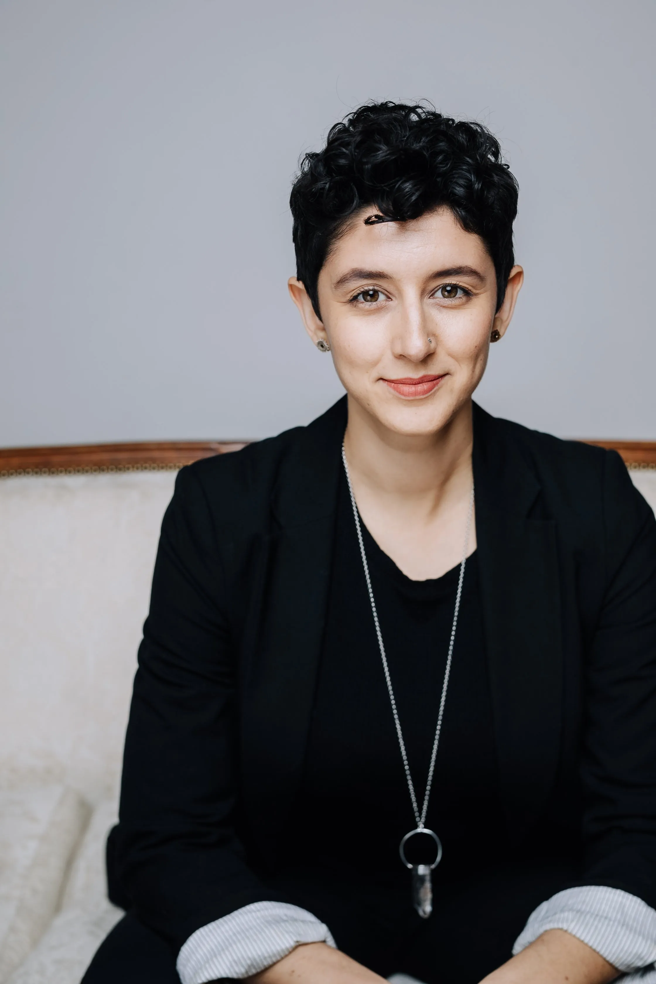 Gillian Cofsky seated, smiling, wearing a black blazer and a long pendant necklace